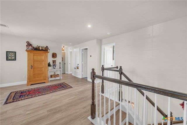 hallway featuring visible vents, an upstairs landing, baseboards, and light wood-type flooring