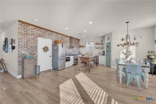 kitchen featuring an inviting chandelier, open shelves, light wood-style floors, appliances with stainless steel finishes, and wall chimney range hood