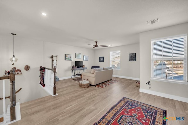 living area with visible vents, light wood-style flooring, baseboards, and ceiling fan