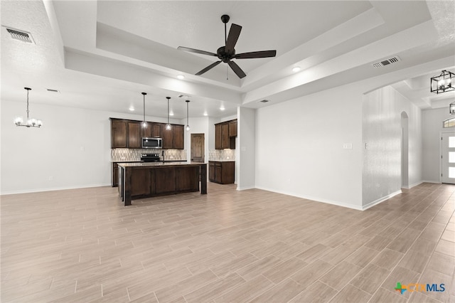 kitchen featuring light hardwood / wood-style flooring, a tray ceiling, decorative light fixtures, and stainless steel appliances