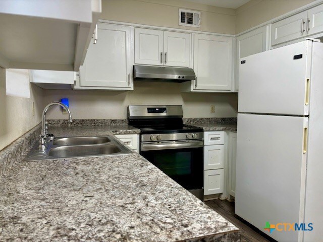 kitchen with white refrigerator, stainless steel range oven, sink, dark hardwood / wood-style floors, and white cabinetry