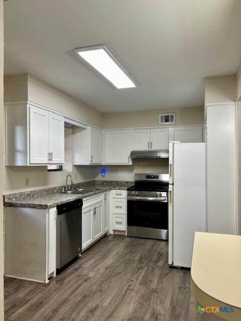 kitchen with dark wood-type flooring, white cabinets, sink, and stainless steel appliances