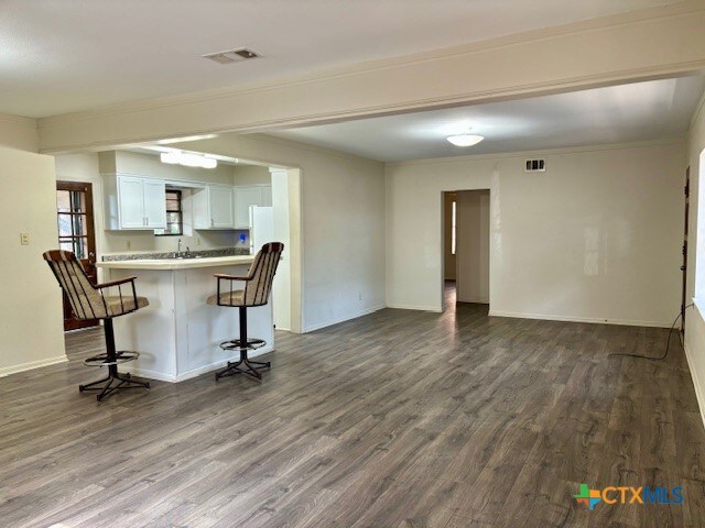 interior space with white cabinetry, kitchen peninsula, ornamental molding, a kitchen bar, and dark hardwood / wood-style floors