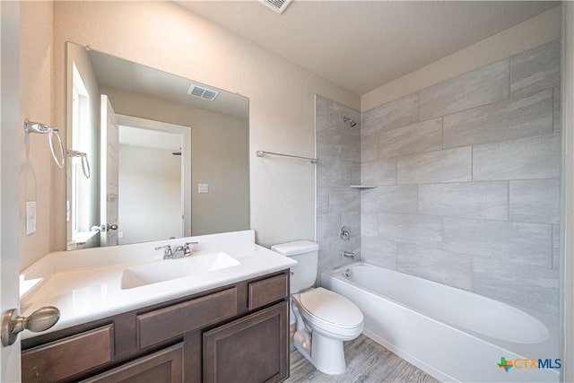 bathroom with wood finished floors, visible vents, toilet, vanity, and tub / shower combination