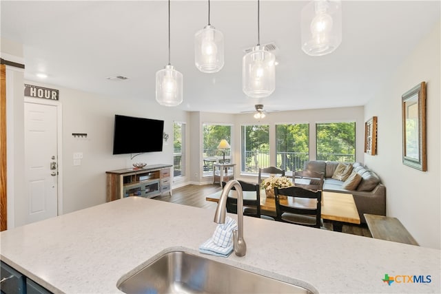 kitchen featuring light stone counters, hardwood / wood-style floors, sink, ceiling fan, and pendant lighting