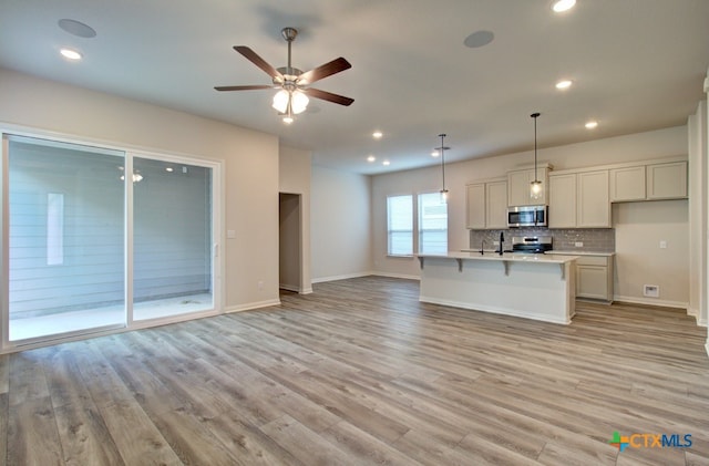 kitchen featuring hanging light fixtures, a center island with sink, light wood-type flooring, and appliances with stainless steel finishes