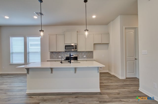 kitchen featuring stainless steel appliances, light hardwood / wood-style floors, hanging light fixtures, and a center island with sink