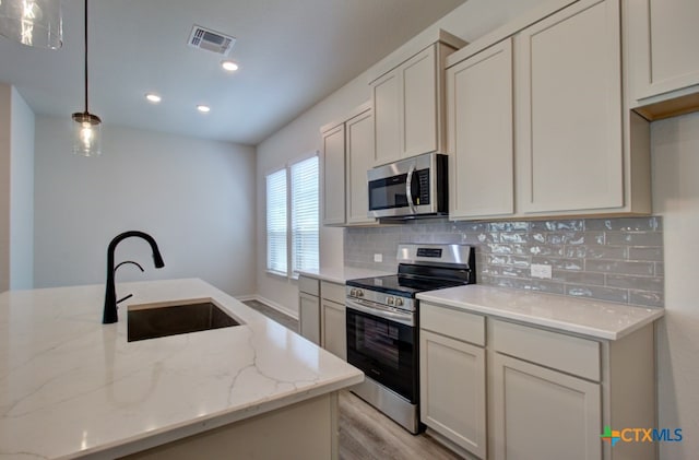 kitchen with sink, appliances with stainless steel finishes, tasteful backsplash, light stone countertops, and pendant lighting