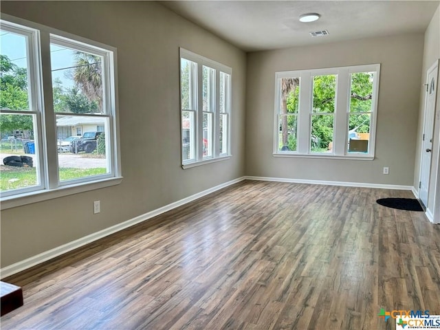 empty room with a wealth of natural light and dark hardwood / wood-style flooring