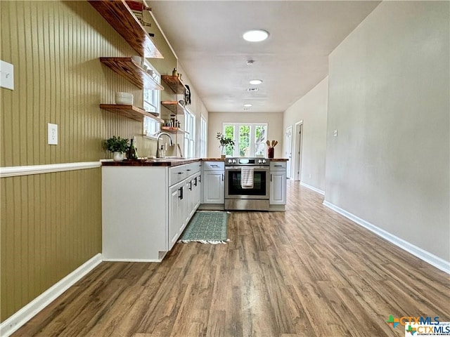 kitchen featuring stainless steel electric range, wood-type flooring, white cabinets, wood walls, and sink