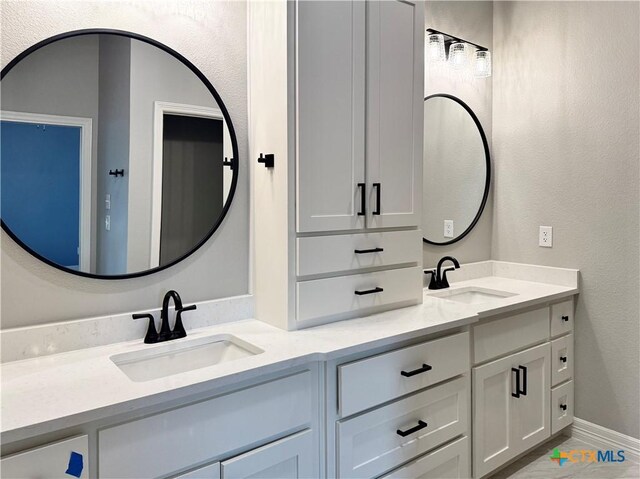 full bath with double vanity, a textured wall, and marble finish floors