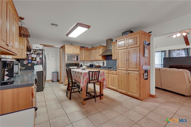 kitchen featuring stainless steel appliances, wall chimney exhaust hood, light tile patterned floors, and ceiling fan