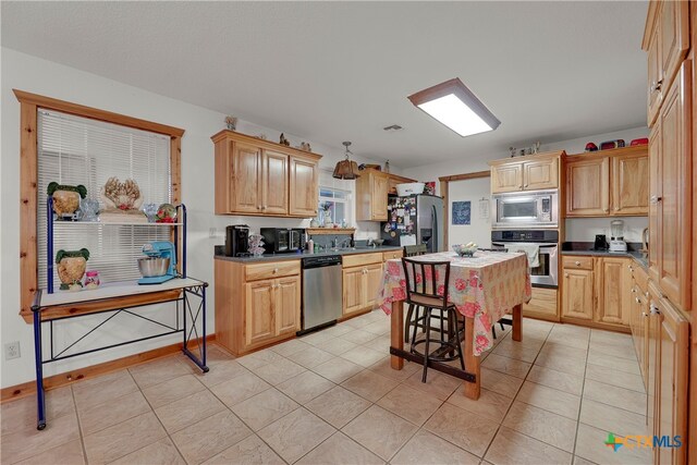 kitchen featuring light brown cabinetry, appliances with stainless steel finishes, light tile patterned flooring, and a center island