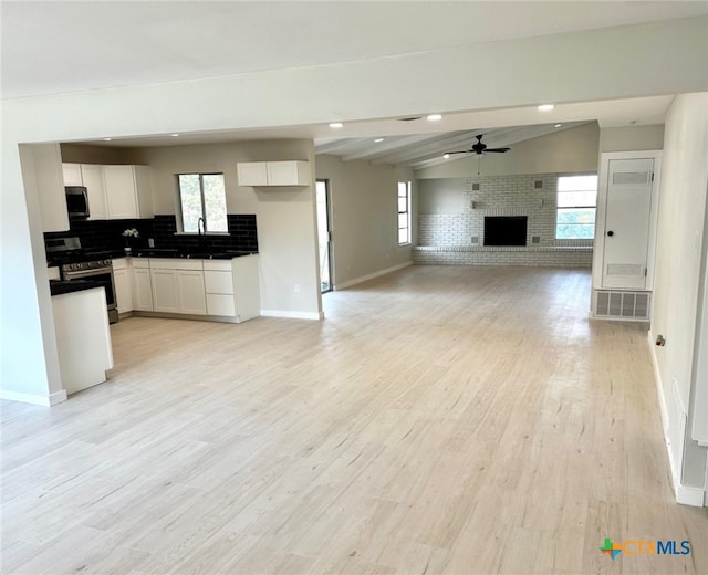 kitchen featuring white cabinets, lofted ceiling with beams, a brick fireplace, light hardwood / wood-style flooring, and stainless steel appliances