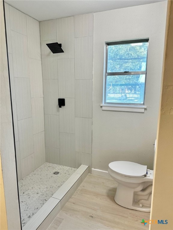 bathroom featuring hardwood / wood-style floors, a tile shower, and toilet