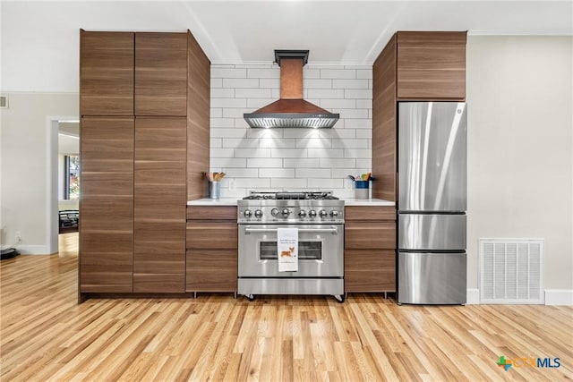 kitchen featuring extractor fan, appliances with stainless steel finishes, tasteful backsplash, ornamental molding, and light hardwood / wood-style floors