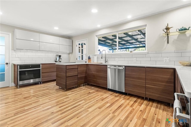 kitchen featuring white cabinetry, backsplash, stainless steel appliances, and light wood-type flooring