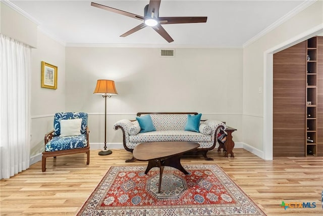 living area with wood-type flooring, ornamental molding, and ceiling fan