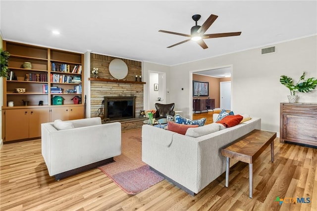 living room featuring ceiling fan, a large fireplace, crown molding, and light wood-type flooring