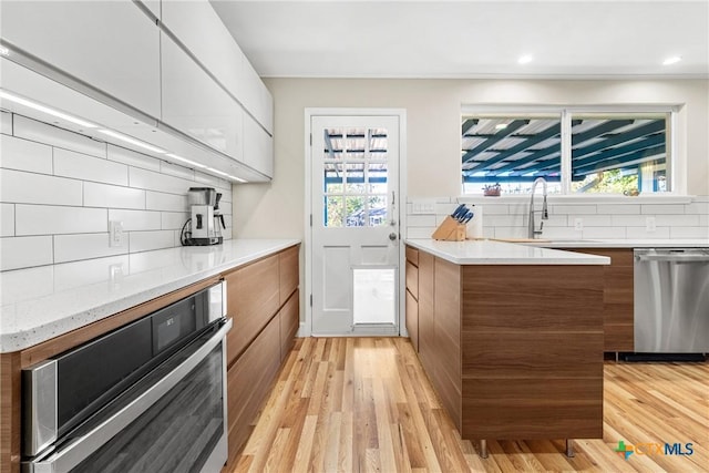 kitchen with dishwasher, sink, white cabinets, decorative backsplash, and light wood-type flooring