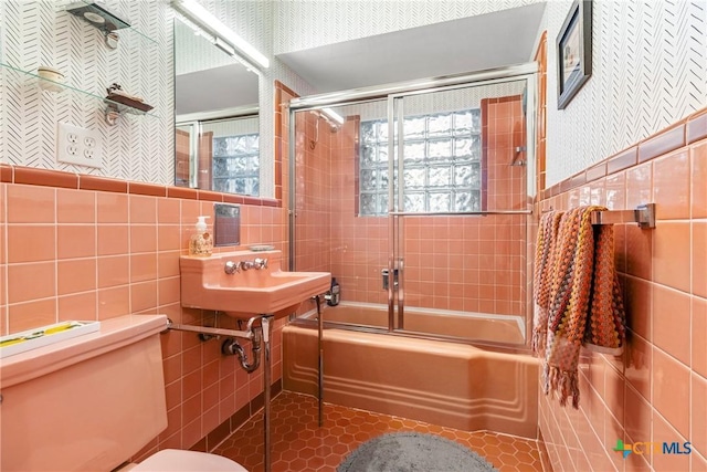 bathroom with tile patterned floors, toilet, combined bath / shower with glass door, and tile walls