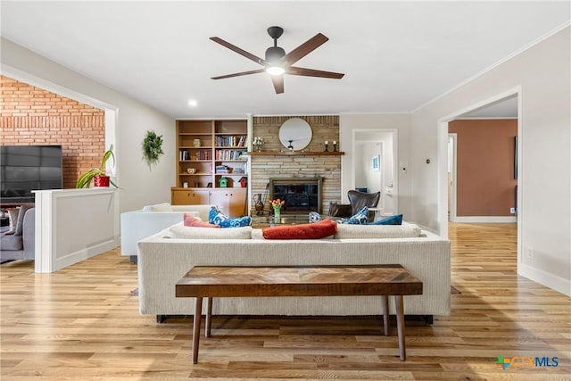 living room featuring crown molding, light wood-type flooring, ceiling fan, and a fireplace