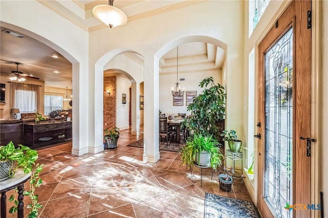 foyer entrance with crown molding, visible vents, a high ceiling, baseboards, and ceiling fan with notable chandelier