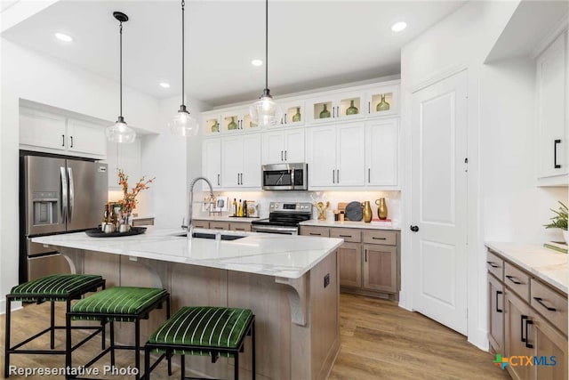 kitchen with a center island with sink, light stone counters, white cabinetry, and appliances with stainless steel finishes