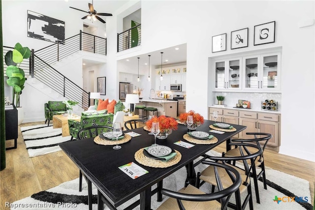 dining room with ceiling fan, a high ceiling, and light wood-type flooring