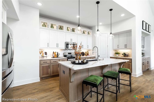 kitchen featuring white cabinets, light stone counters, an island with sink, and appliances with stainless steel finishes