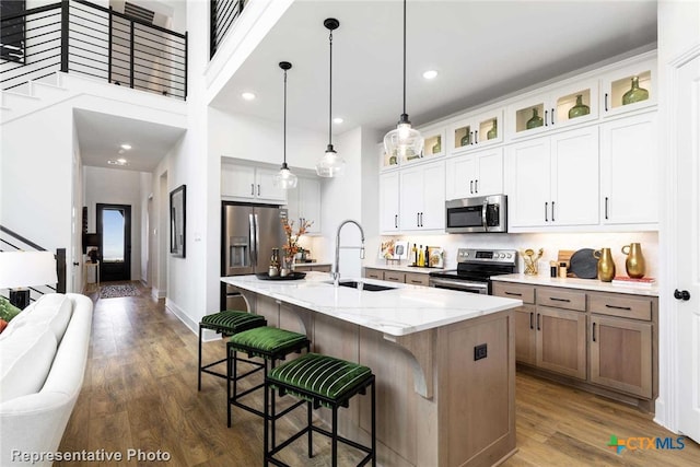 kitchen featuring a center island with sink, white cabinets, sink, appliances with stainless steel finishes, and light stone counters