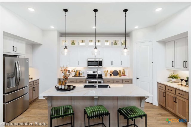 kitchen featuring light stone counters, a center island with sink, white cabinets, and stainless steel appliances