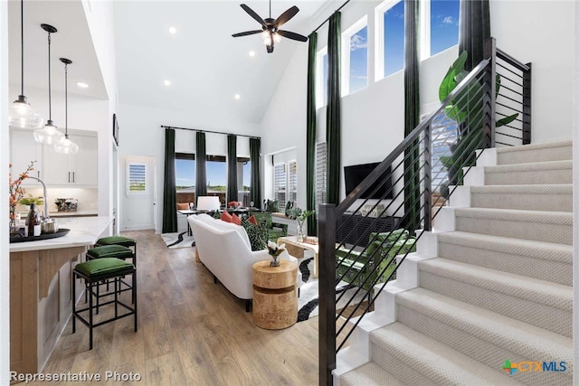 living room featuring ceiling fan, a towering ceiling, a healthy amount of sunlight, and hardwood / wood-style flooring