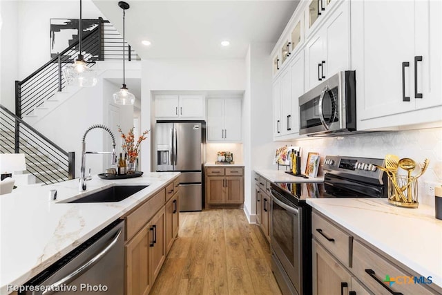 kitchen with white cabinets, hanging light fixtures, sink, appliances with stainless steel finishes, and light hardwood / wood-style floors