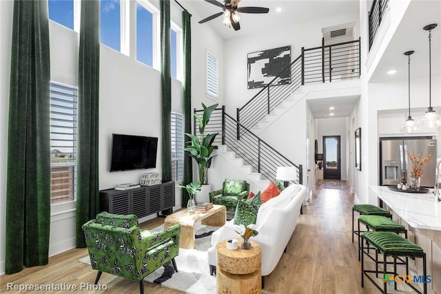 living room with ceiling fan, a towering ceiling, and light hardwood / wood-style flooring