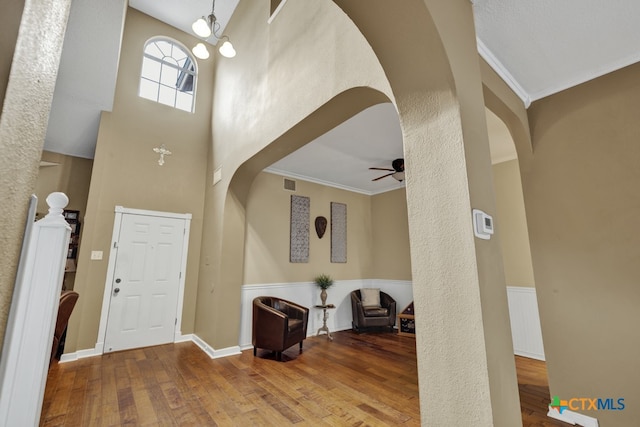 entryway featuring ornamental molding, ceiling fan with notable chandelier, hardwood / wood-style flooring, and a high ceiling