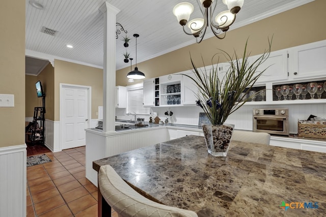 kitchen with stainless steel oven, hanging light fixtures, crown molding, and white cabinets