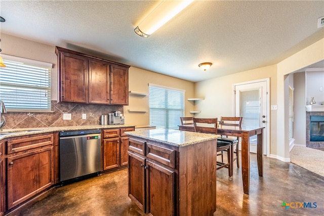 kitchen featuring a textured ceiling, sink, dishwasher, a tile fireplace, and a center island