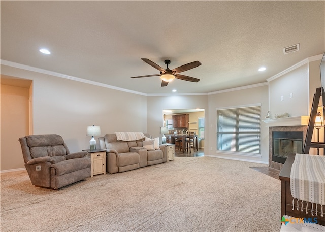 carpeted living room with ceiling fan, a textured ceiling, a tiled fireplace, and crown molding