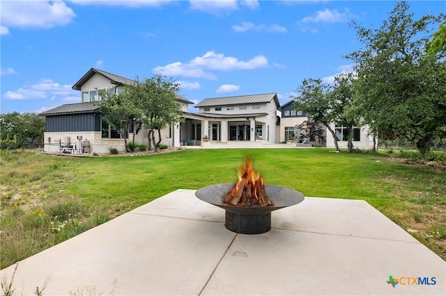 rear view of property featuring an outdoor fire pit, a lawn, metal roof, a standing seam roof, and a patio area