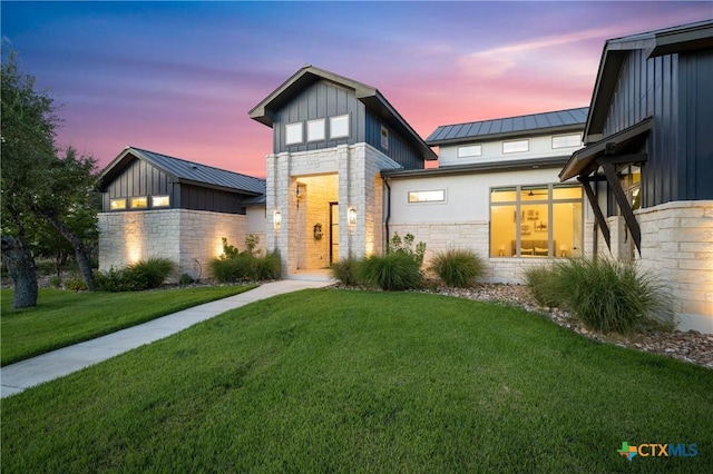 view of front of property with metal roof, stone siding, a lawn, board and batten siding, and a standing seam roof