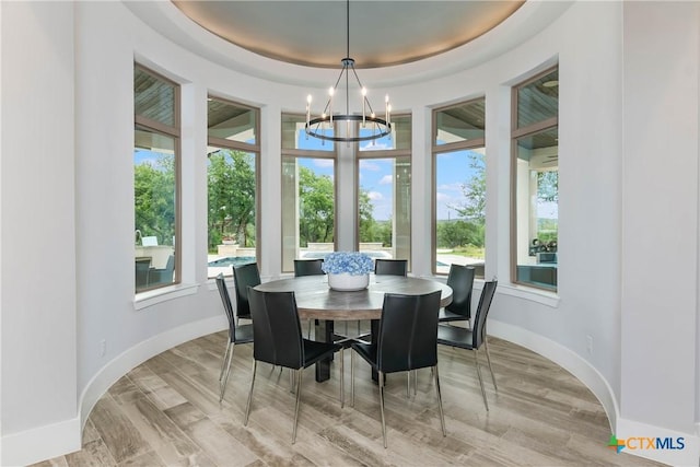 dining area featuring baseboards, light wood-style flooring, a tray ceiling, and a notable chandelier