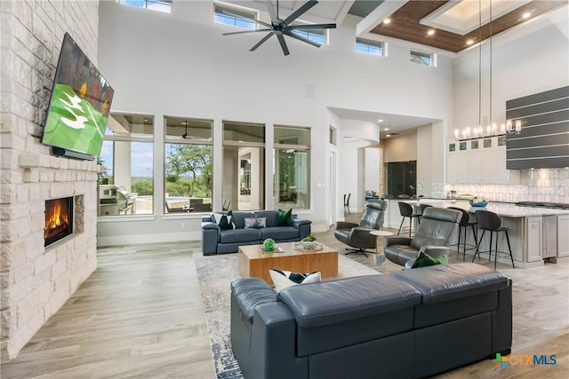 living area featuring light wood-style flooring, a fireplace, beam ceiling, and a ceiling fan