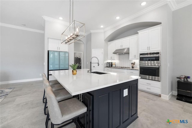 kitchen featuring a kitchen bar, sink, a large island with sink, appliances with stainless steel finishes, and decorative backsplash