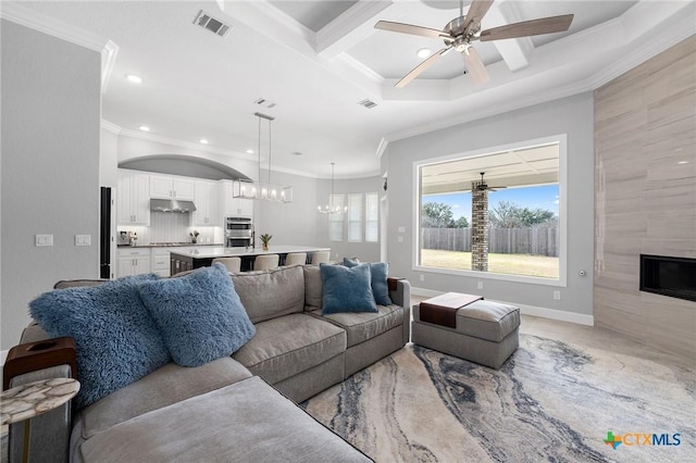 living room with a tiled fireplace, crown molding, coffered ceiling, and ceiling fan with notable chandelier