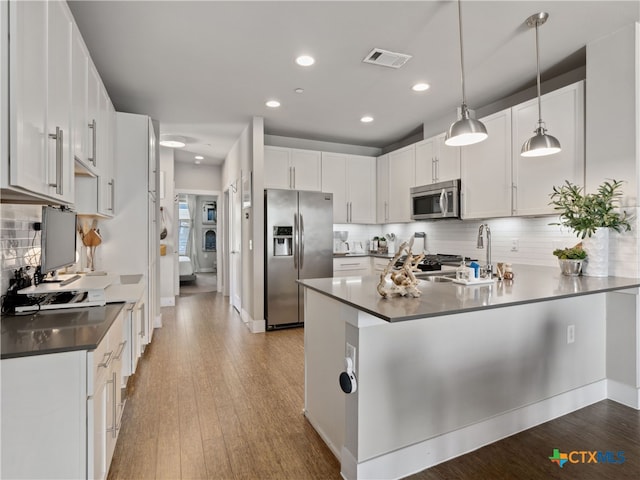 kitchen featuring white cabinets, kitchen peninsula, stainless steel appliances, and hanging light fixtures