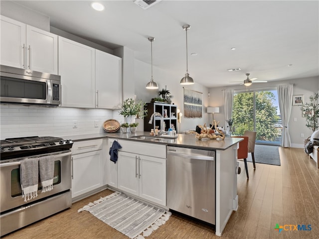 kitchen with stainless steel appliances, white cabinetry, light wood-type flooring, pendant lighting, and kitchen peninsula