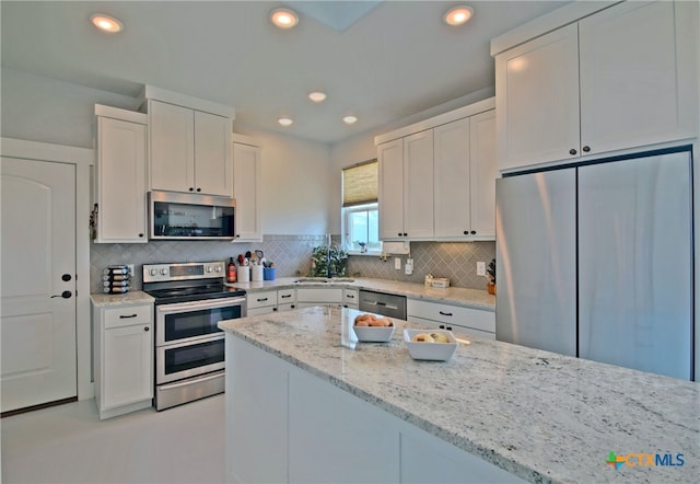 kitchen featuring decorative backsplash, appliances with stainless steel finishes, light stone counters, sink, and white cabinets