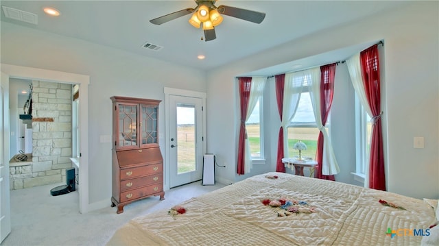 carpeted bedroom with access to exterior, ceiling fan, and a stone fireplace