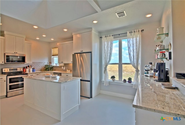 kitchen with backsplash, white cabinetry, stainless steel appliances, and light stone counters